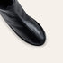 Close-up of a black leather ankle boot showing the side profile and toe, set against a solid off-white background.