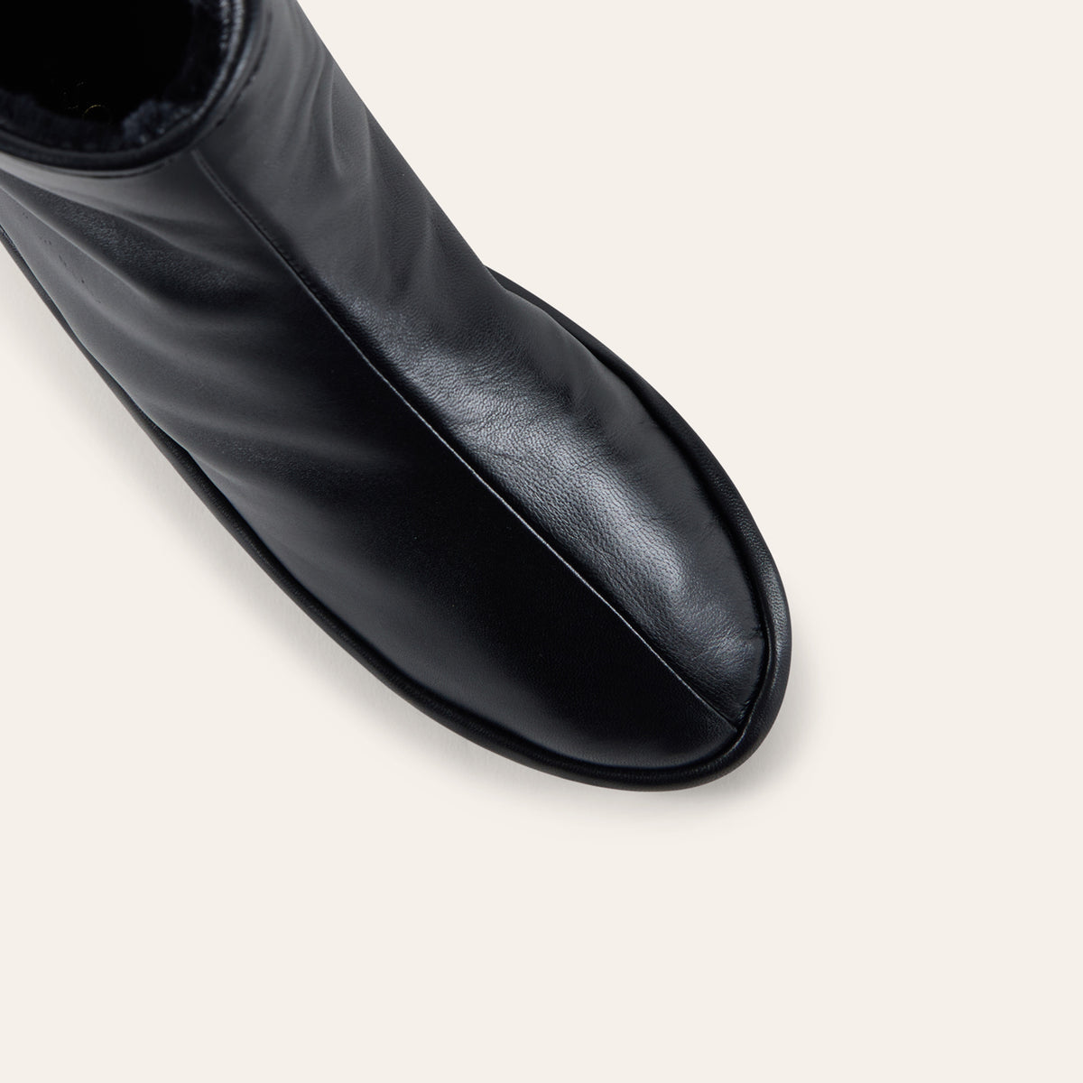 Close-up of a black leather ankle boot showing the side profile and toe, set against a solid off-white background.