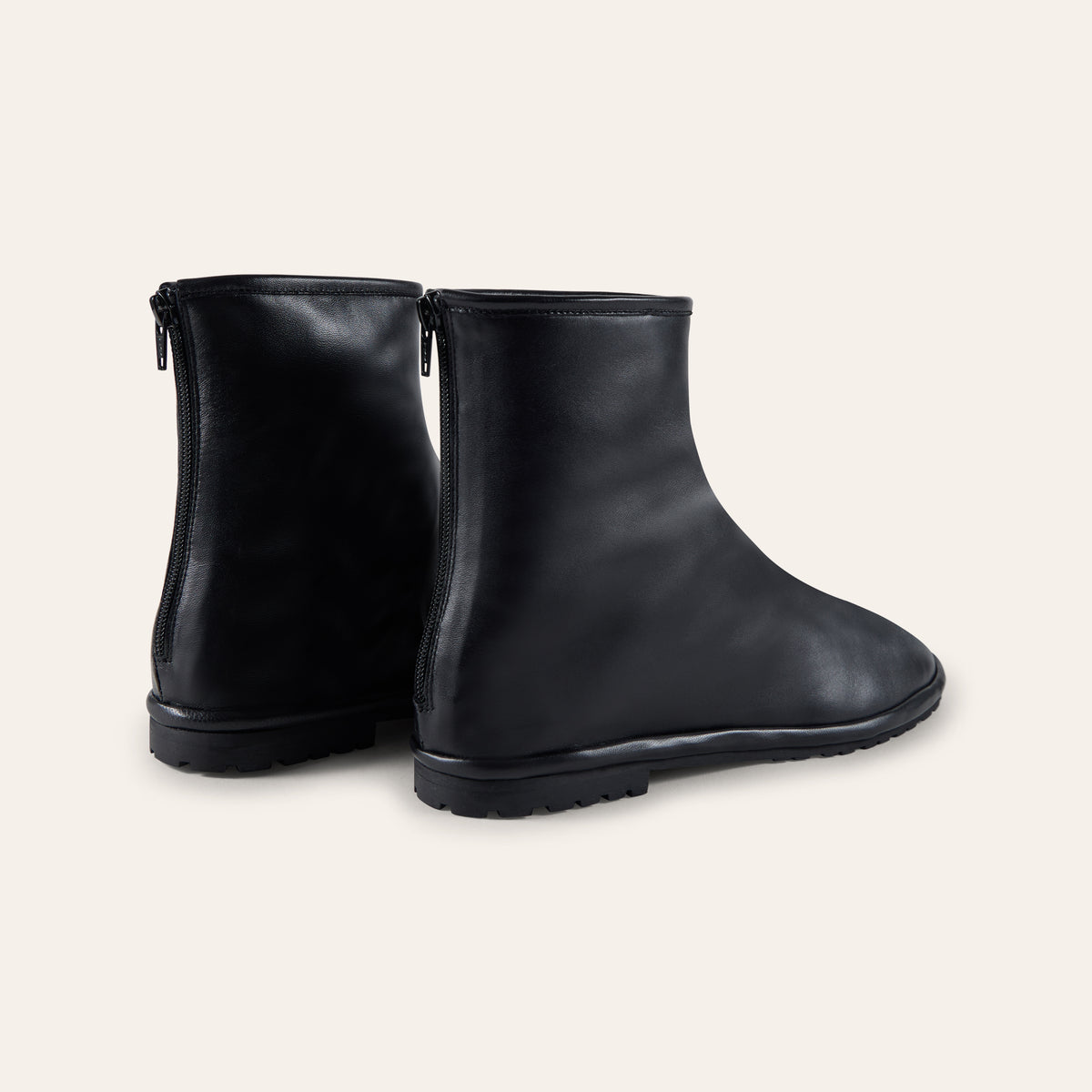 A pair of black leather ankle boots with side zippers, shown from a three-quarters angle on a light beige background.