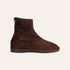 A dark brown suede ankle boot with a side zipper, shown in profile against a light cream background.