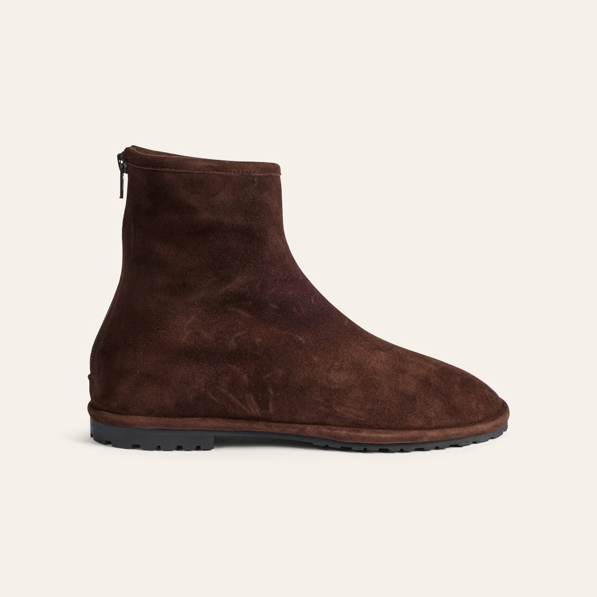 A dark brown suede ankle boot with a side zipper, shown in profile against a light cream background.