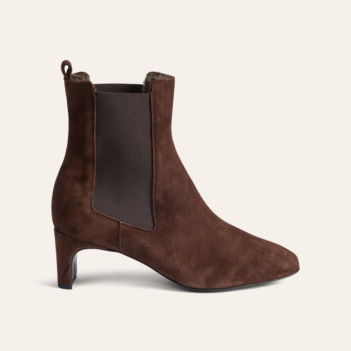 A single brown suede Chelsea-style ankle boot with a pointed toe and a low block heel, shown in profile against a light cream background.