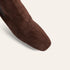 Close-up of a dark brown suede boot with a square toe, shown against a light beige background.