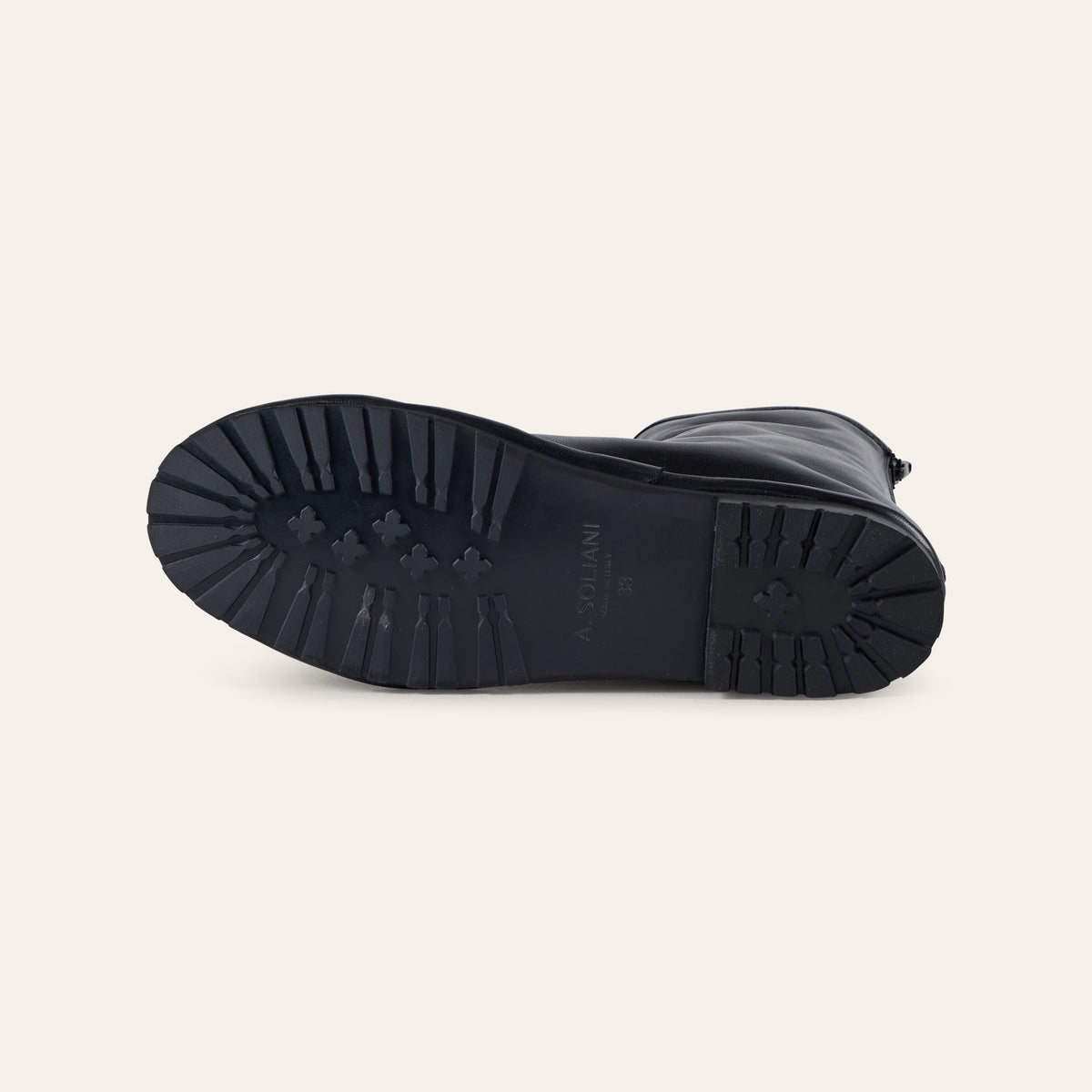 A close-up of the black rubber outsole of a boot, showing the tread pattern and embossed brand name, photographed on a light beige background.
