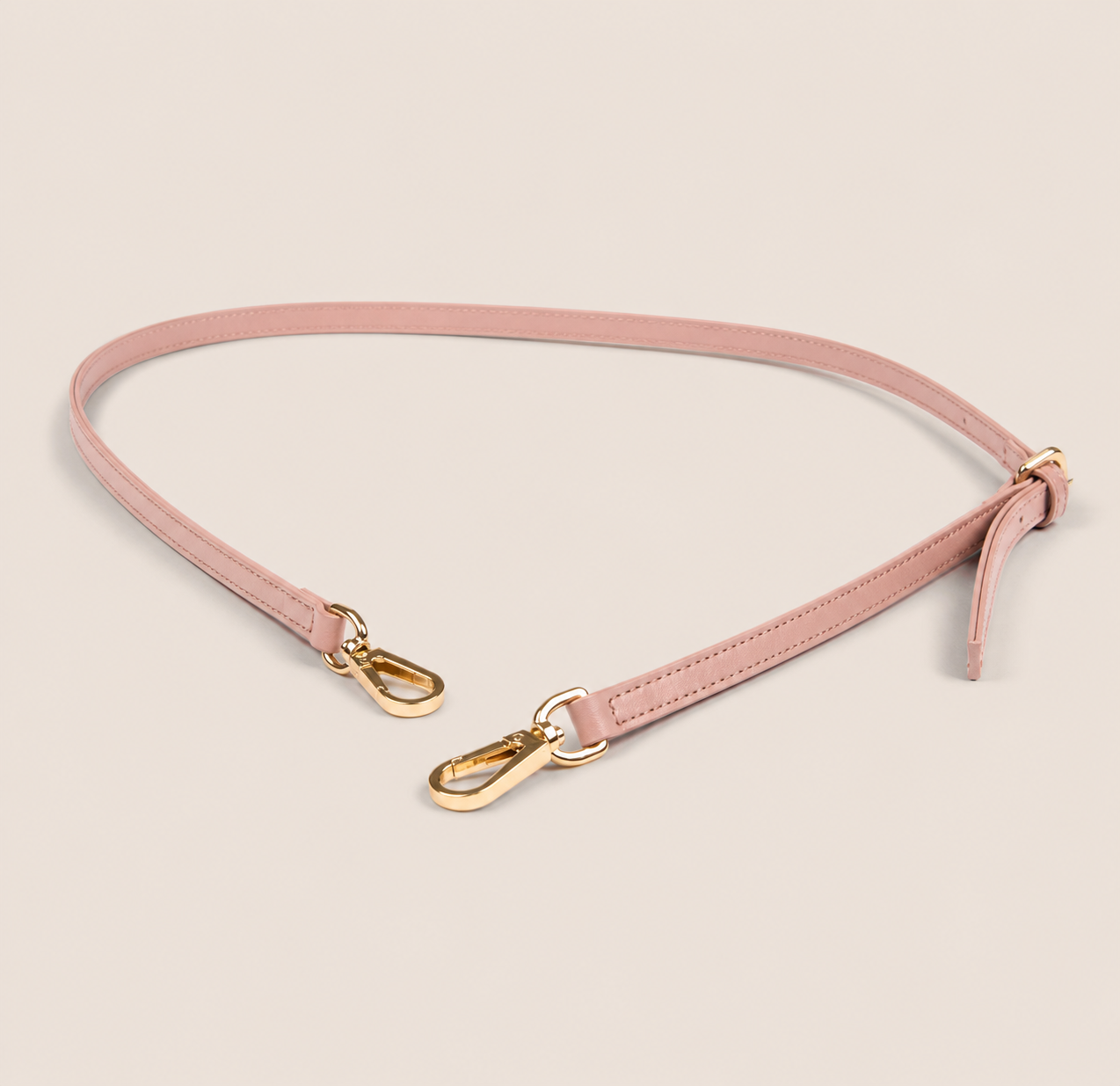 Pink shoulder strap with gold hardware on a beige background