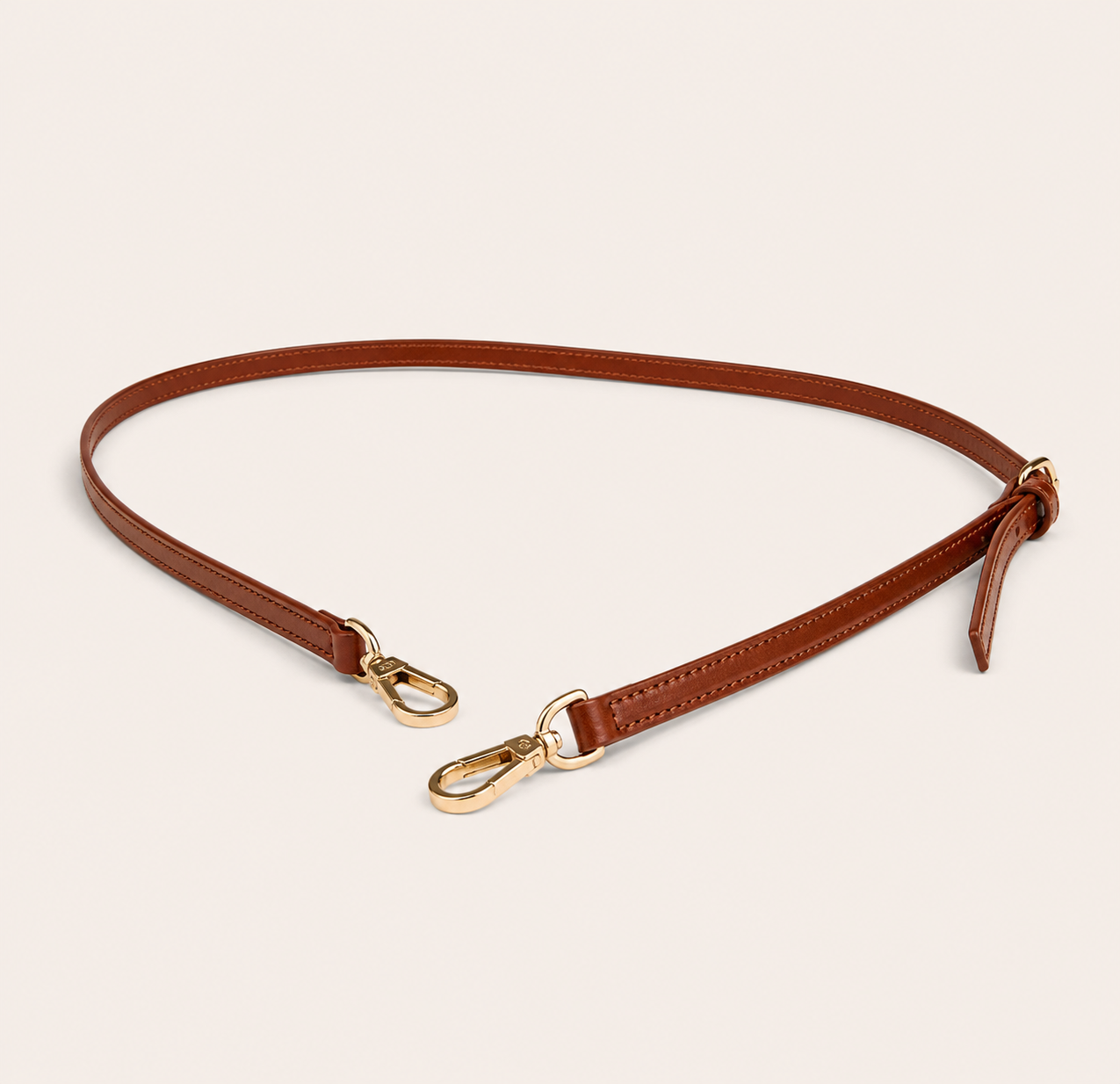 Brown leather shoulder strap with gold hardware on a beige background