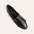 A single black leather loafer with fringe detailing on the toe, shown from a top-down angle on a light beige background. The brand name 'A.