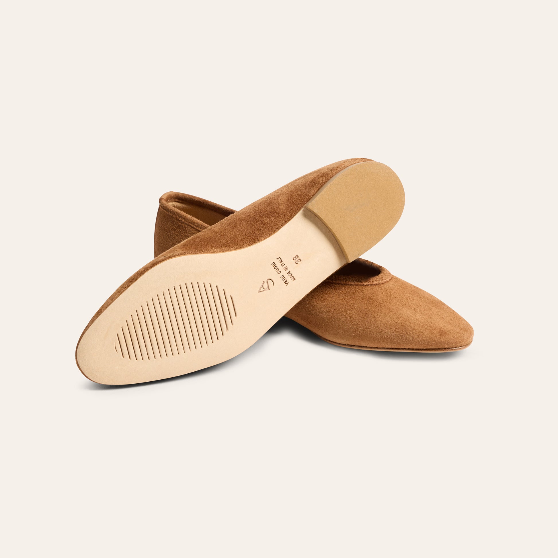 A pair of tan suede pointed-toe flats shown from a top-down angle, displaying the beige outsole with size and brand markings, set against a solid off-white background.