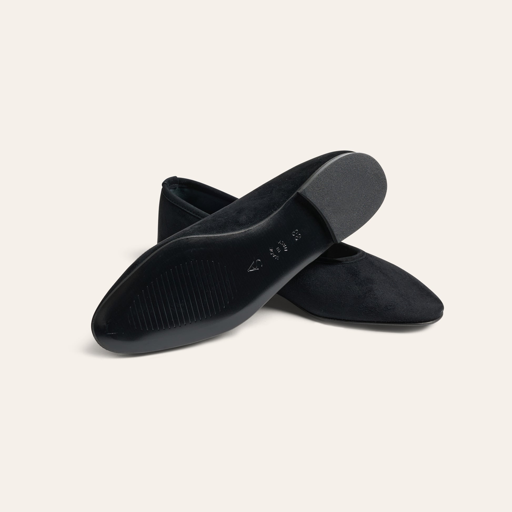 A pair of black pointed-toe flats shown from a top-down angle, set against a solid off-white background.