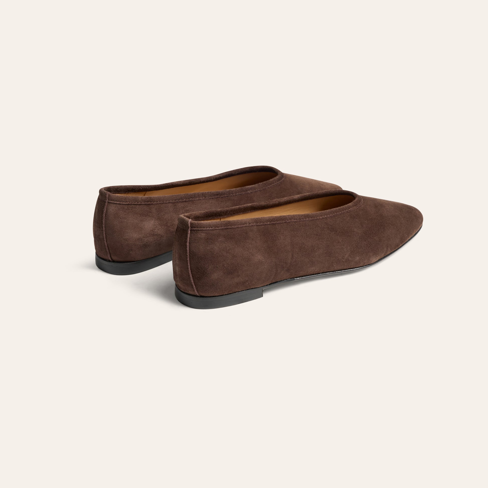 A pair of dark brown suede slip-on flats with pointed toes, shown from a three-quarters angle on a light cream background.