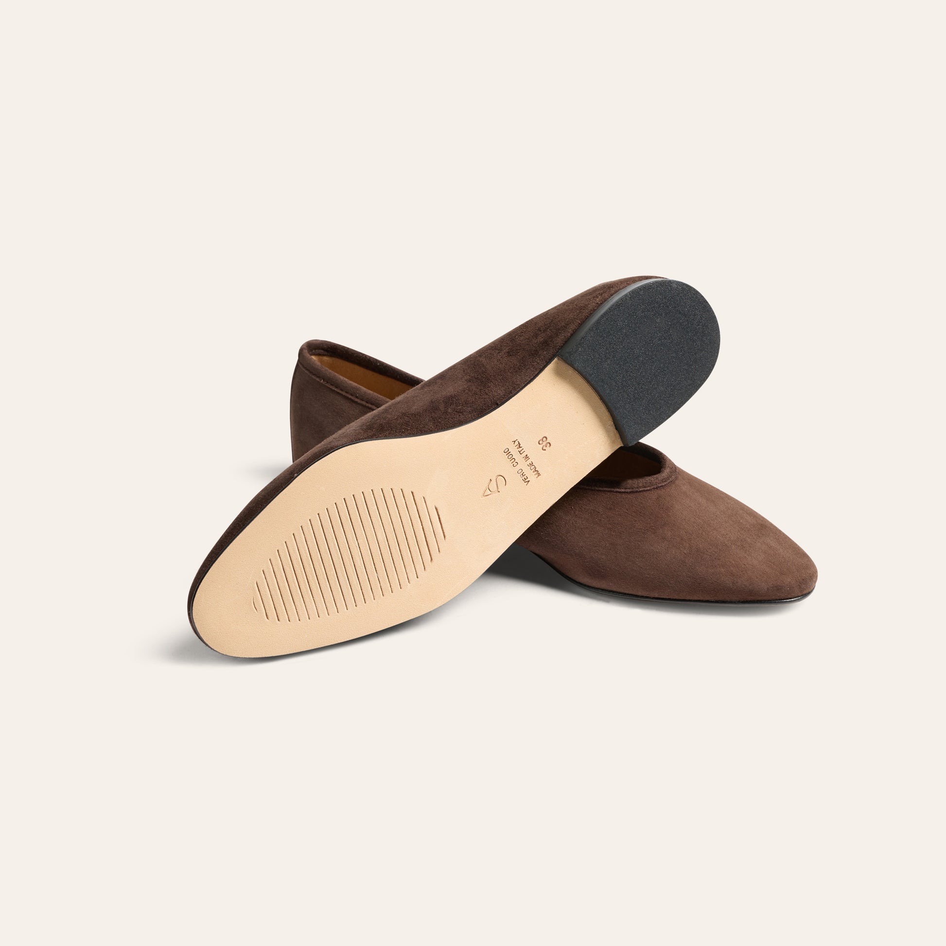 A pair of dark brown suede pointed-toe flats shown from the side, with one shoe turned to display the beige insole and black outsole.