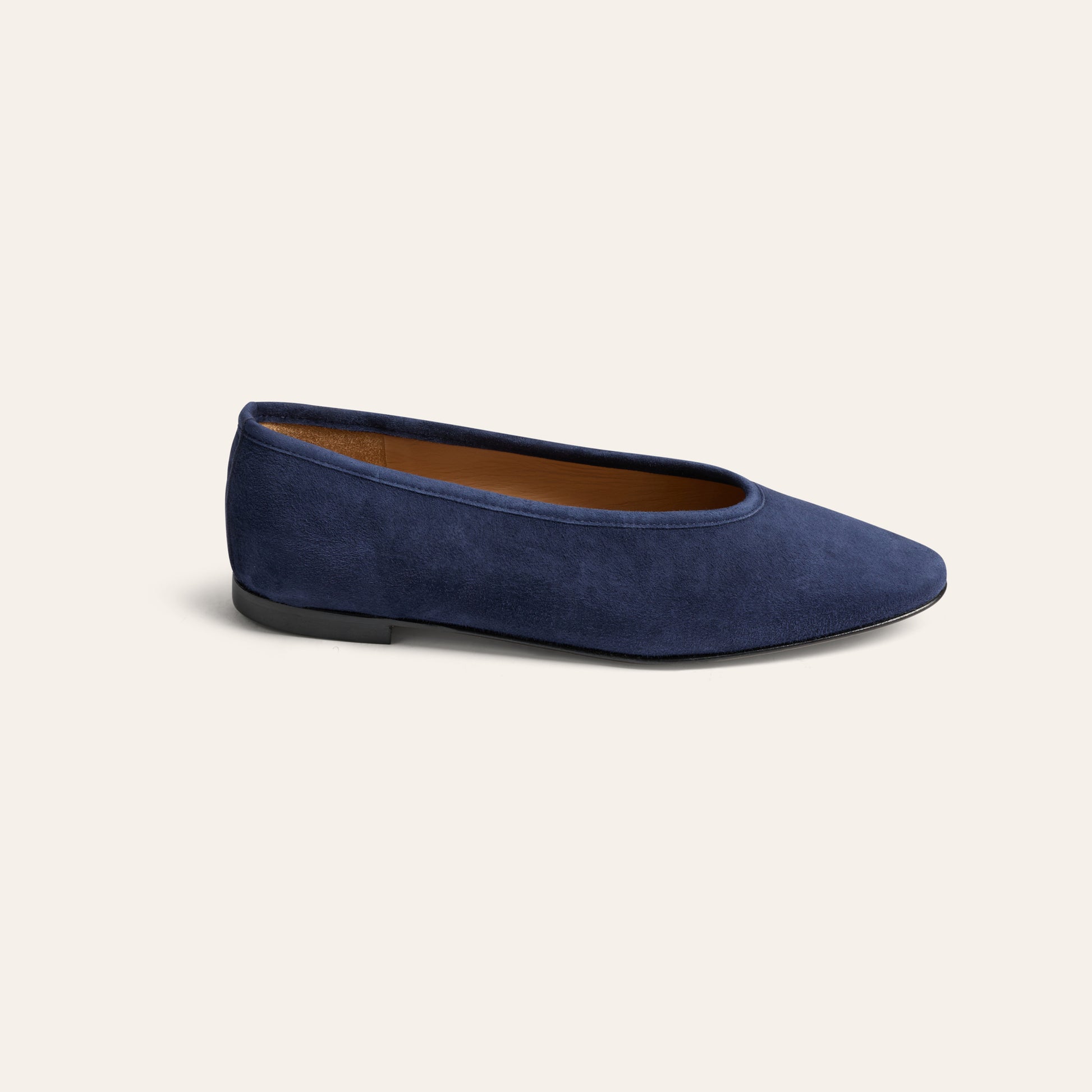 A single navy blue suede flat shoe with a pointed toe and a tan interior lining, shown from a side profile on a light cream background.