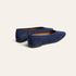 A pair of navy blue suede flat shoes with black soles, shown from a three-quarters angle on a light beige background.