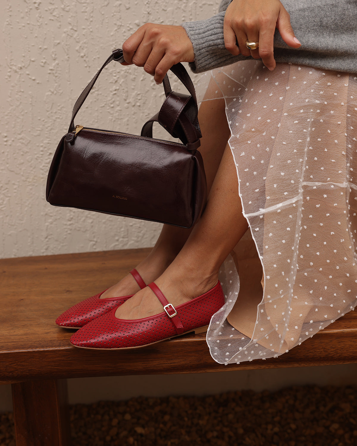 Person wearing red shoes and holding a brown handbag, sitting on a wooden bench.